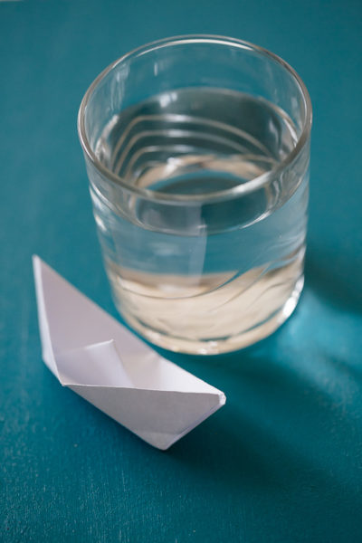 Un bateau en papier à côté d'un verre d'eau