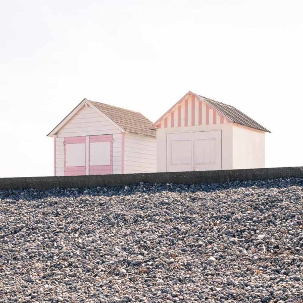 Deux cabines de plage blanches et roses et plage de galets.